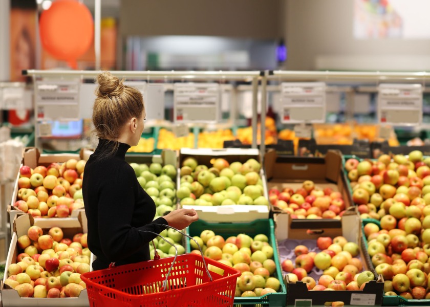 A woman with a bun stands in front of a display of apples, considering her choice.